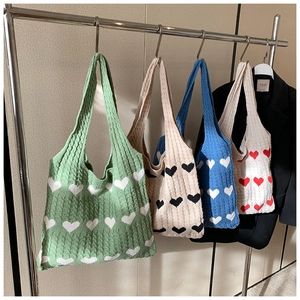 Detail view of four colorful knitted heart tote bags hanging on a metal rack