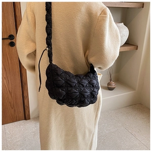 Detailed view of a black quilted cloud crossbody bag on a model wearing a beige coat