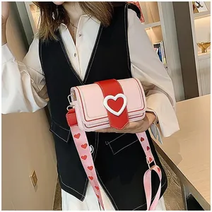 Détail du sac bandoulière rose et rouge avec fermoir cœur et large bandoulière imprimée