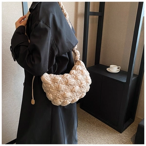 Detail view of beige quilted shoulder bag with textured pleats and thick strap on model