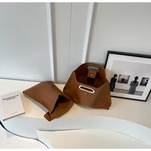 Detail of a brown leather tote set with oval cutout handle on a minimalist white surface
