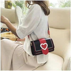 Détail d'un sac bandoulière noir avec une grande boucle en cœur rouge et une large sangle