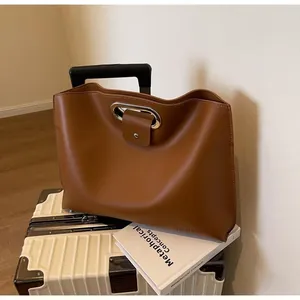 Close-up of brown leather tote bag with silver oval handle on ivory suitcase