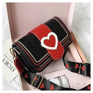 Détail du sac bandoulière à motif cœur dans sa boîte cadeau avec large sangle décorée