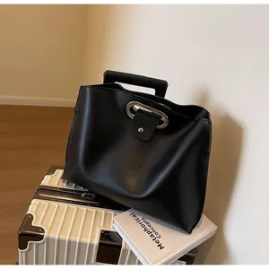 Detail of black leather tote bag with metal ring handle on luggage and art book