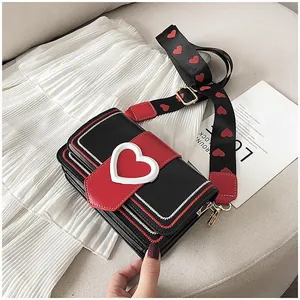 Détail du sac à main cœur rouge et noir avec large bandoulière à motifs et boucle