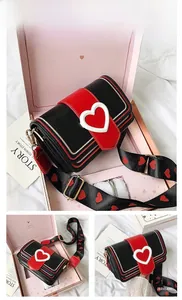 Détail du sac bandoulière noir avec fermoir cœur rouge et large bandoulière assortie