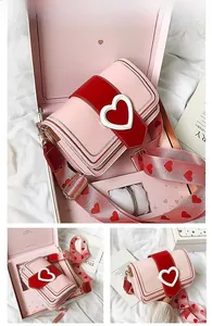 Détail du sac bandoulière rose en forme de cœur avec sangle décorée et boîte cadeau