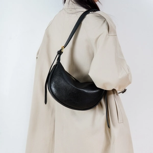 Minimalistische schwarze Hobo-Tasche mit Faltenstruktur am Model in beigem Mantel