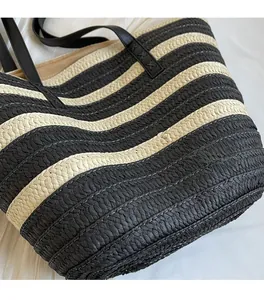 Detailed macro view of woven wave patterns and black leather handles on straw tote bag