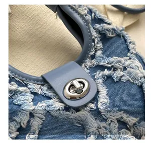 Detail of silver twist lock on light blue denim bag with fringe texture and tassel finish