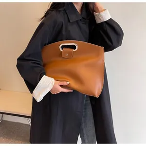 Detail of a brown leather tote bag with unique silver metal cutout handles and snap closure