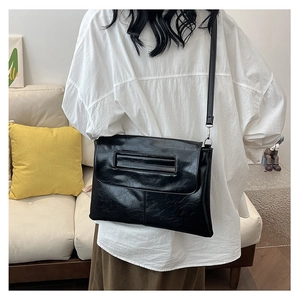 Shoulder bag showing black glossy wrinkled texture and crossbody wear style