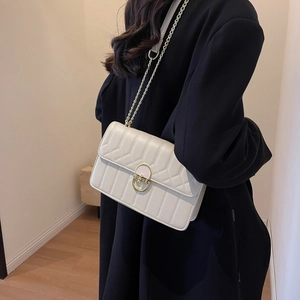 Minimalistische cremeweiße Stepptasche mit goldener Kette getragen auf schwarzem Mantel