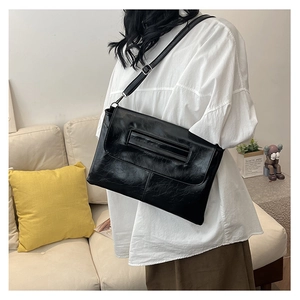 Detail of minimalist black glossy PU leather envelope bag with adjustable shoulder strap