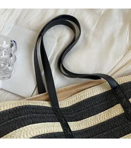Detail of reinforced black leather shoulder strap and woven texture on a straw tote bag