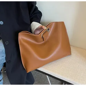 Detail view of large brown leather tote bag with stylish metal ring closure and text