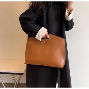 Detail of large brown leather tote with circular metal handle and pressed logo