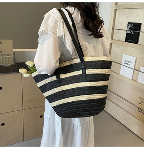 Detail of a large black and white striped woven tote bag with leather shoulder straps