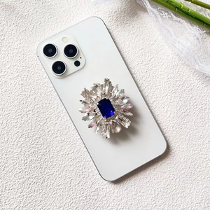 Detail of luxury rhinestone phone grip with blue emerald-cut gem and crystals
