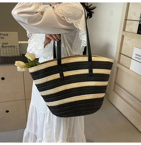 Detail of large woven straw tote bag featuring black and white stripes and leather handles
