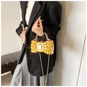 Detail of golden bow-shaped metal clutch bag with a sleek metallic handle and chain strap