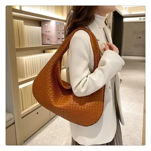 Vista laterale della borsa hobo intrecciata caramello con ampia tracolla su modella