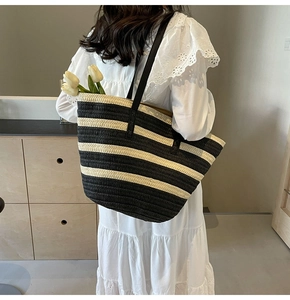 Detail of striped straw tote bag featuring black leather straps and textured weaving