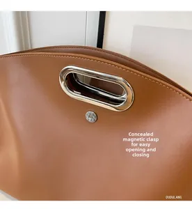 Detail of brown litchi leather tote featuring oval metal handle and hidden magnetic closure