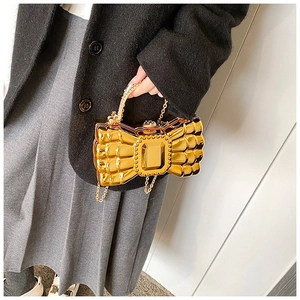 Detail of a shiny gold bow-shaped evening clutch bag with chain strap and jeweled handle