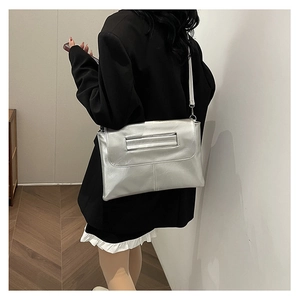 Rear view of model wearing a silver envelope clutch bag with metal strap on shoulder