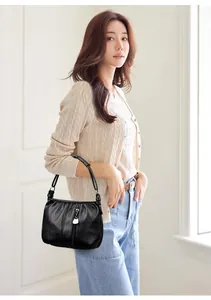Asian model holding a textured black PU leather handbag in bright indoor lighting