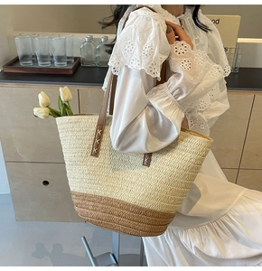 Detail of two-tone woven straw tote bag with brown leather handles and X-shaped stitching