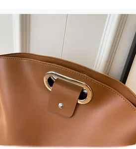 Detail of brown leather tote featuring silver U-shaped metal handles and matte texture