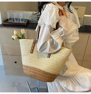 Detail of color-block straw tote bag with brown leather handles and white stitching
