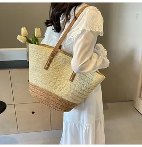 Detail of straw tote bag showing brown leather strap with decorative white cross-stitching