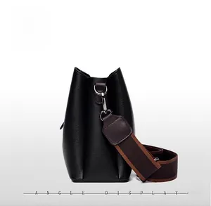 Side view of black pebbled leather bucket bag with contrasting brown wide fabric strap