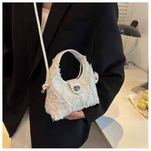 Detail of white quilted denim crossbody crescent bag with frayed edges and metal clasp