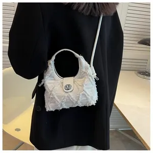 Detail of white quilted canvas crossbody bag with frayed fringe edges and metal lock
