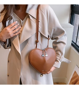 Détail d'un sac en cuir marron en forme de cœur avec un zip trèfle et une finition mate
