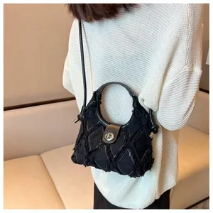 Close-up of quilted denim crescent bag featuring frayed edges and silver metal buckle