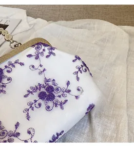 Detail of vintage gold metal clasp and purple floral embroidery on white lace bag