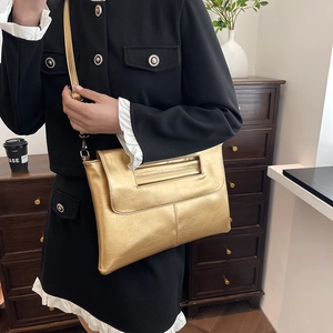 Chic gold metallic clutch bag with cutout handle and shoulder strap worn by a model