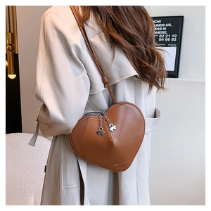 Détail du sac à bandoulière cœur en cuir marron avec zips trèfle sur un trench-coat élégant