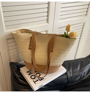 Detail of two-tone woven straw tote bag with brown leather handles and white stitching
