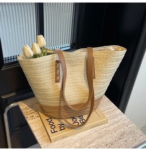 Detail of handwoven straw tote bag with brown leather strap and contrast stitching