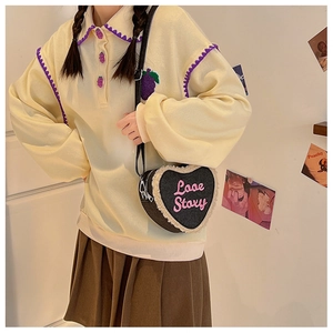 Détail du sac à bandoulière en forme de cœur avec broderie Love Story porté par un mannequin
