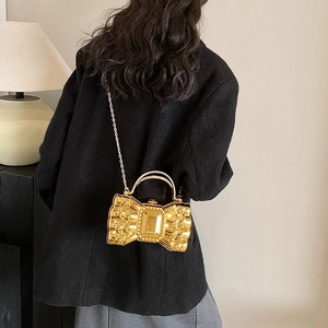Elegant gold bow-shaped hardshell evening bag with chain strap shown on a black coat