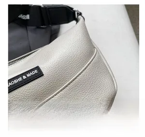Detail of cream textured leather crossbody bag showing brand label and fabric strap