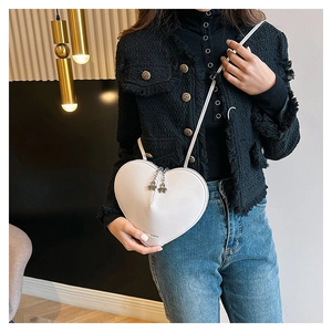 Détail du sac à bandoulière blanc en forme de cœur avec pendentif trèfle en métal